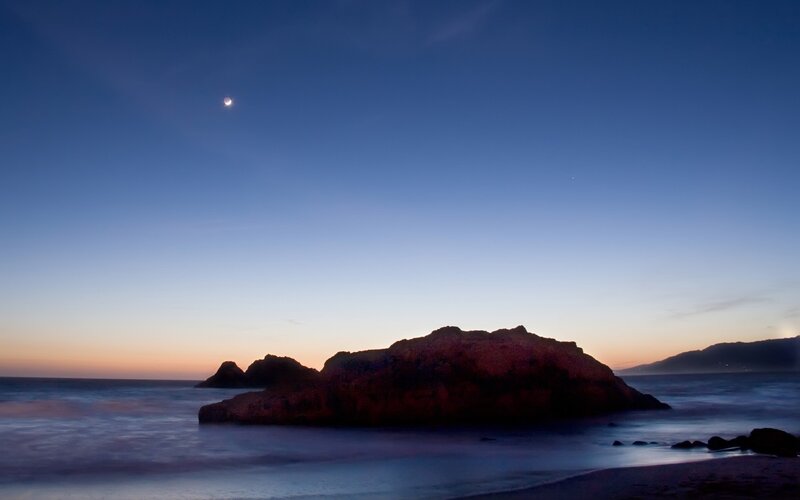 Moon over coastal rocks at dusk