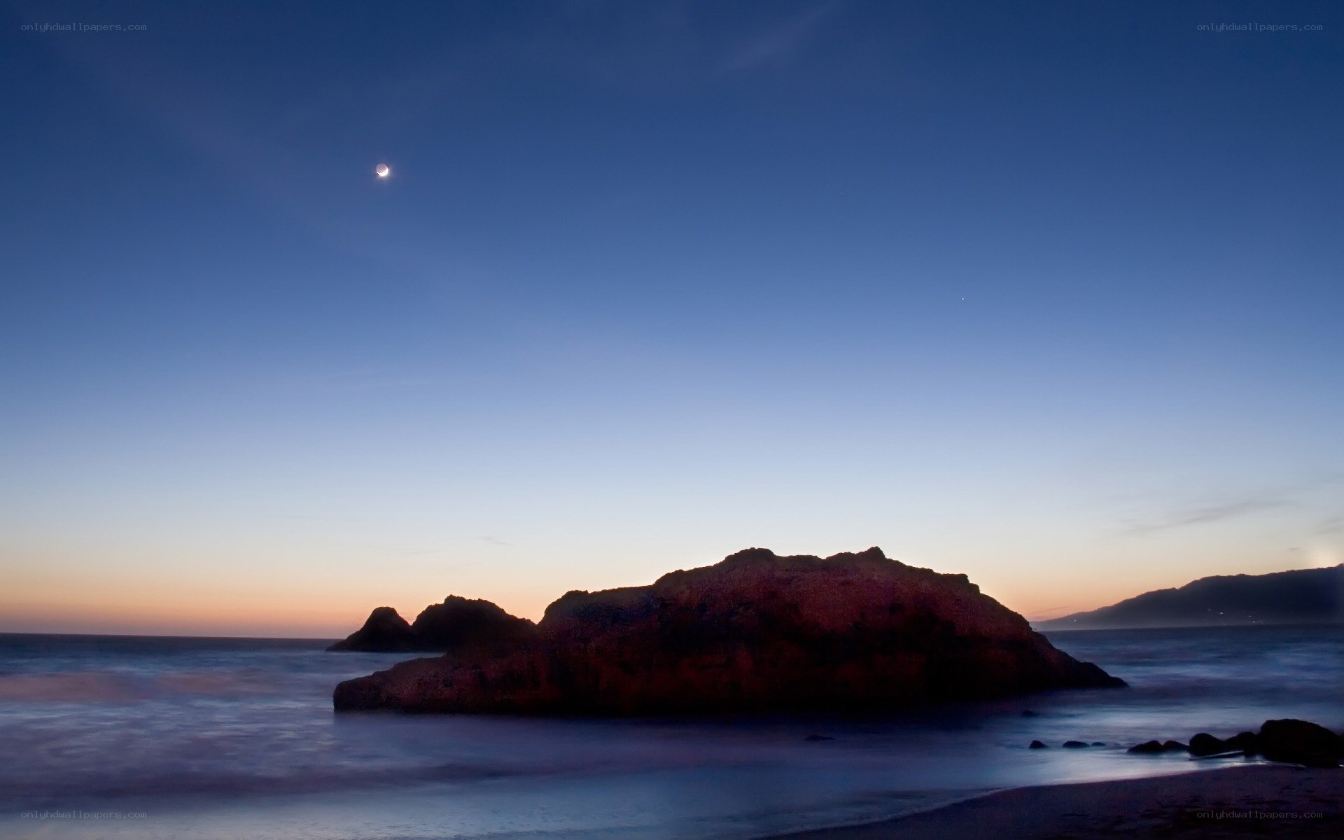Moon over coastal rocks at dusk