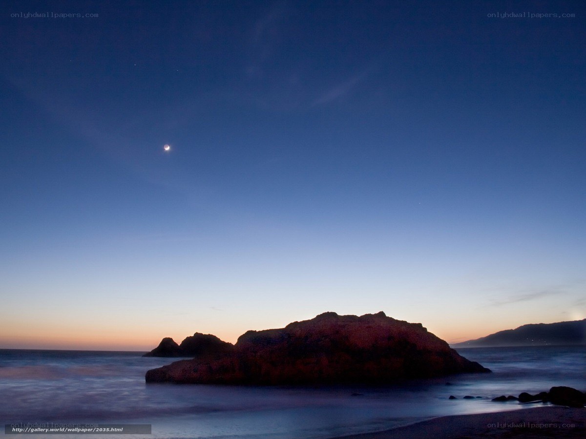 Moon over coastal rocks at dusk