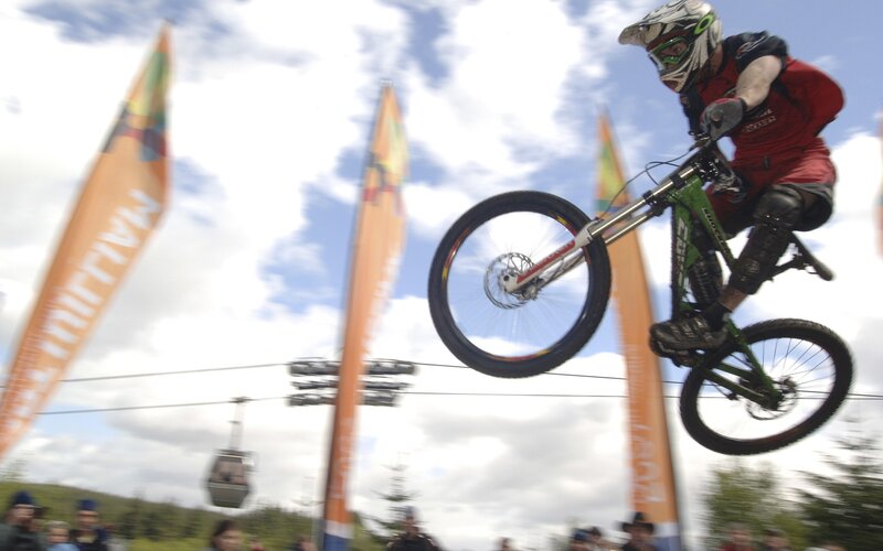 Mountain Biker in Mid-air — Green, Dynamic, Afternoon, Photograph, Bicycle, Helmet, Flags