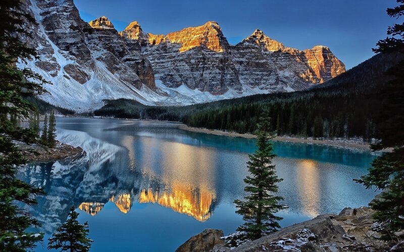 Mountain Lake Reflection — Blue, Serene, Sunset, Photograph, Snow-capped Mountains, Evergreen Trees, Calm Water, Gold, White