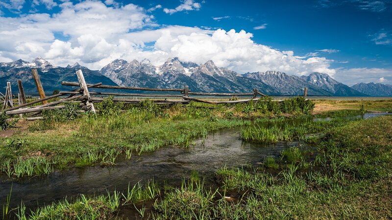 Mountain Range with Stream — Blue, Serene, Afternoon, Photograph, Fence, Clouds, Grass, Green, Gray
