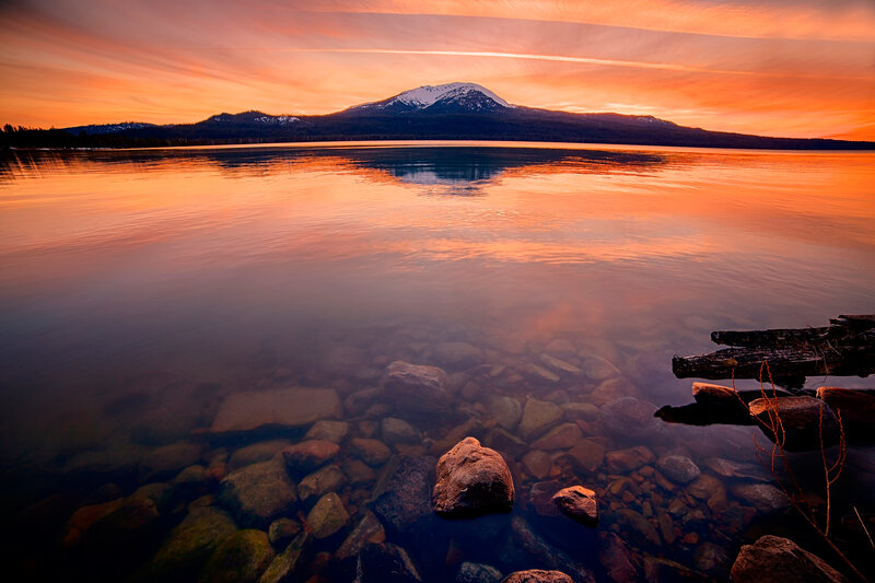 Mountain Reflected in Lake — Orange, Serene, Sunset, Photograph, Rocks, Driftwood