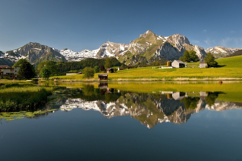 Mountain Reflection in Lake — Blue, Serene, Afternoon, Photograph, Mountains, Grass, Huts