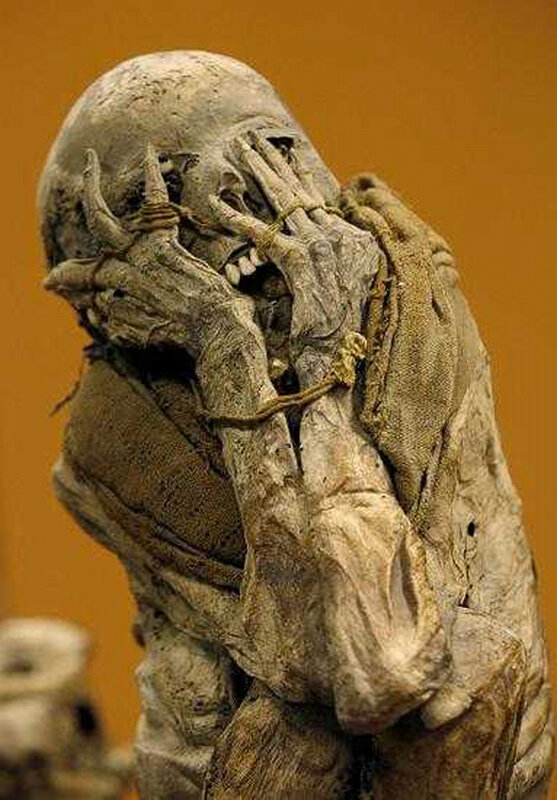 Mummified figure with hands covering face