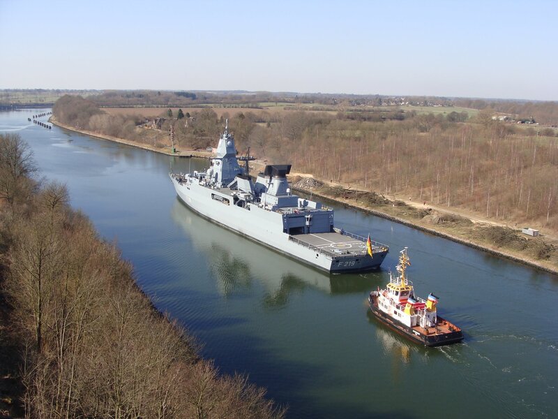 Naval ship in canal with tugboat