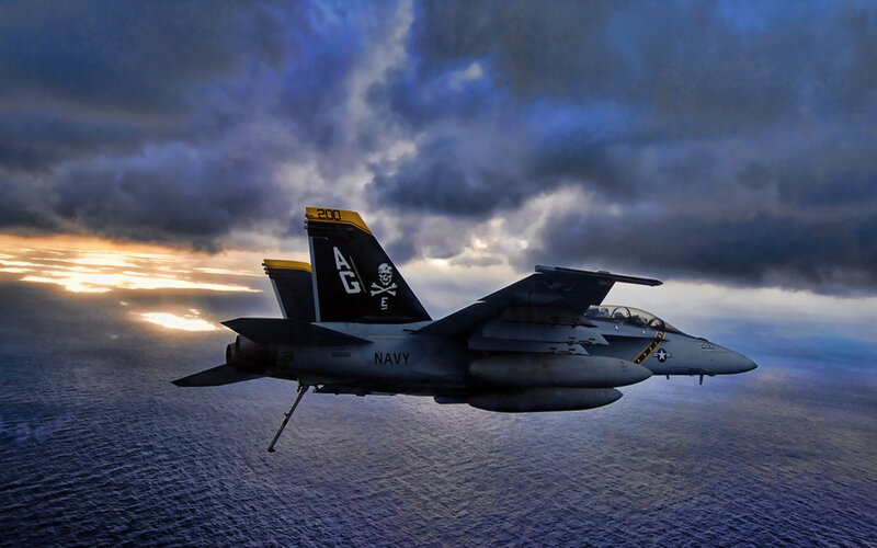 Navy jet over ocean at sunset