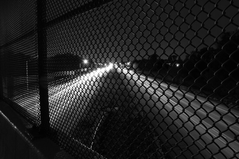 Nighttime highway through chain-link fence