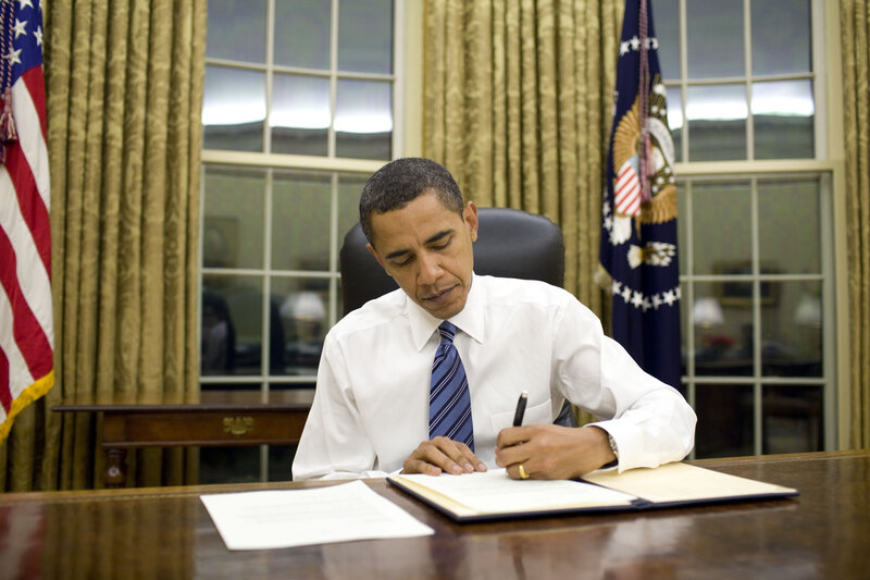Obama signing document at desk