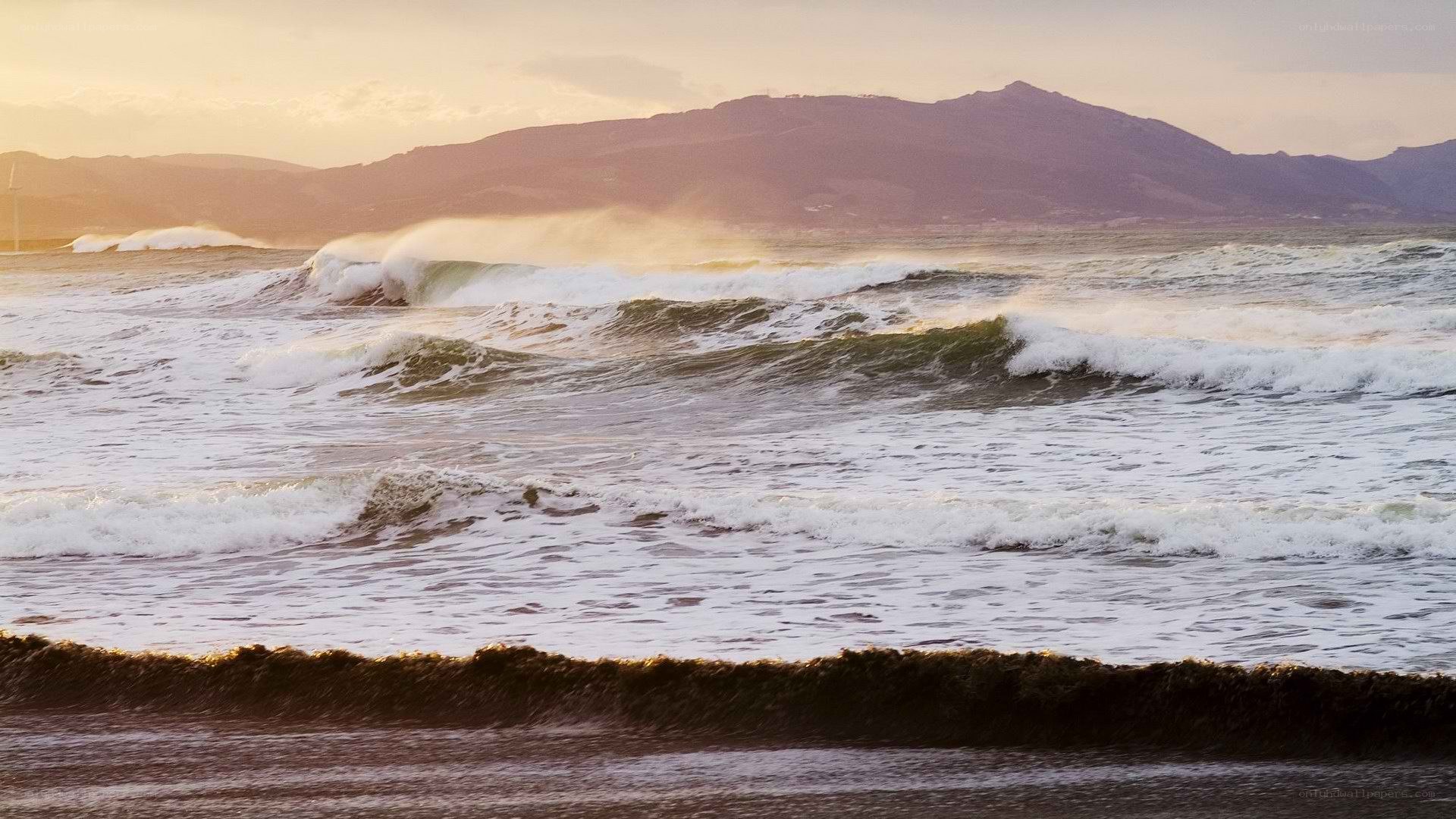 Ocean waves at sunset with mountains