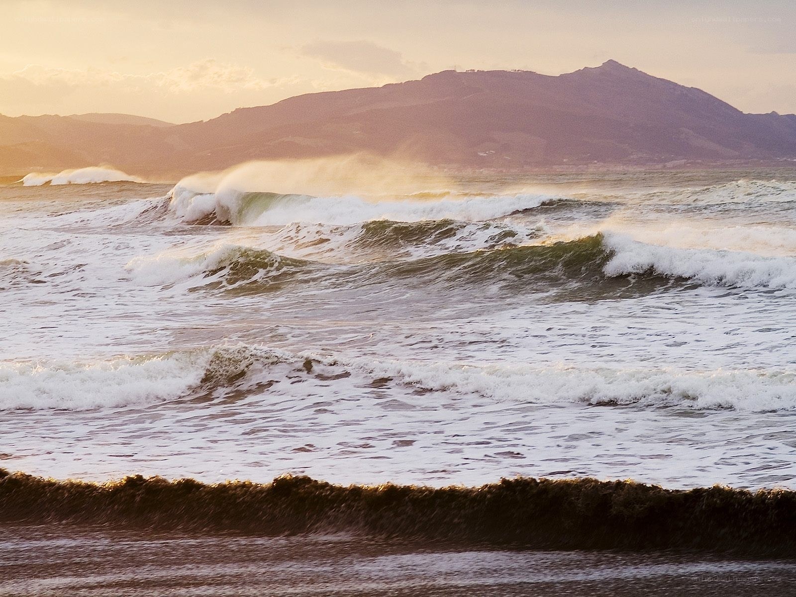 Ocean waves at sunset with mountains