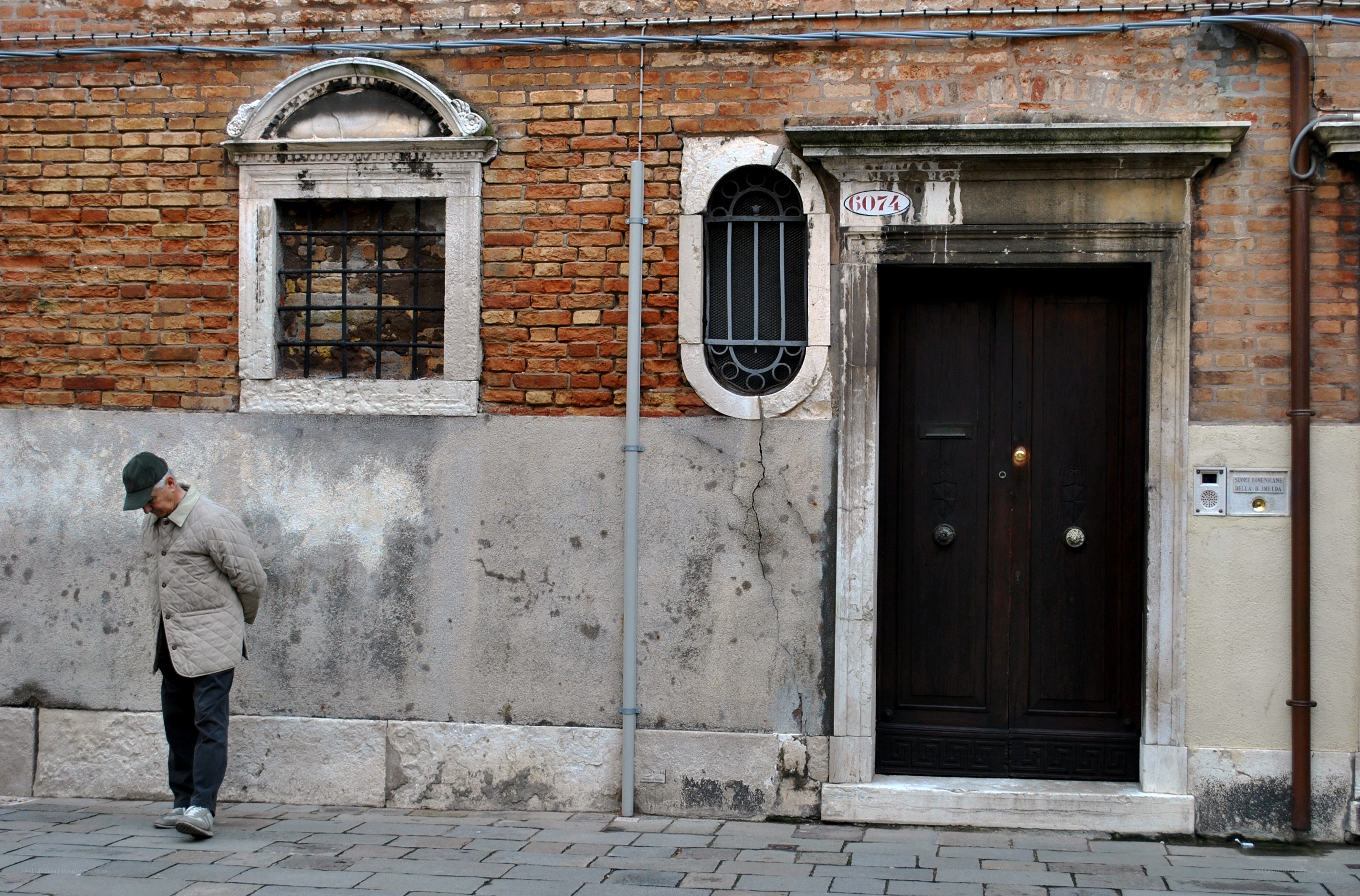 Old man walking past a brick building