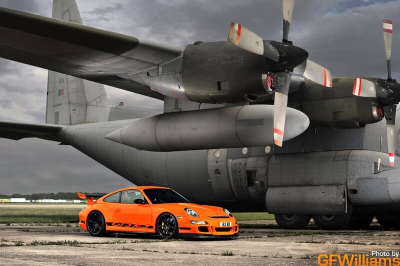 Orange Porsche next to military plane