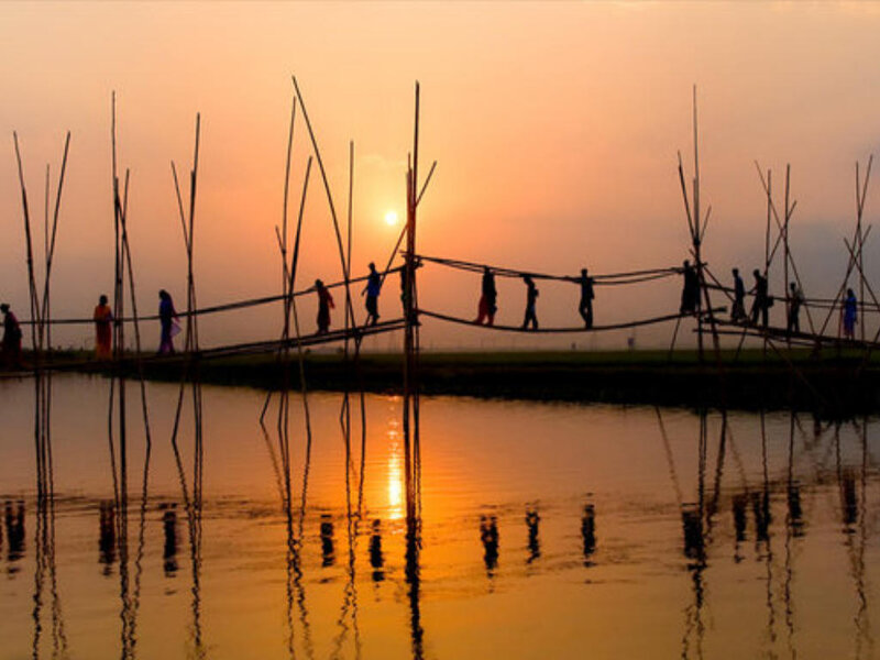 People crossing a bamboo bridge at sunset