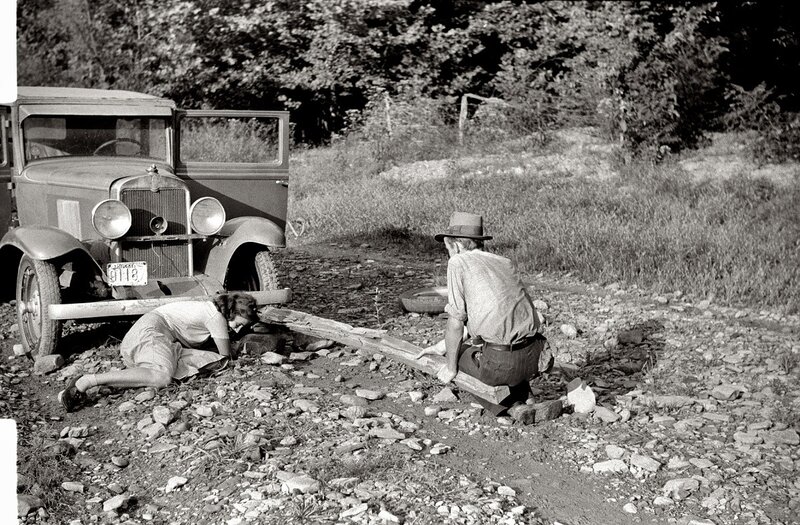 People fixing a car on a dirt road