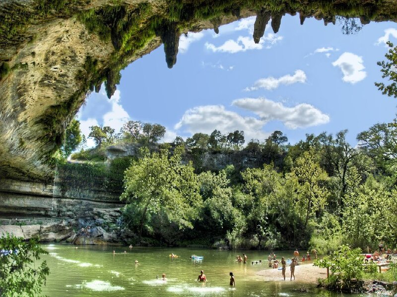 People swimming under a natural rock arch