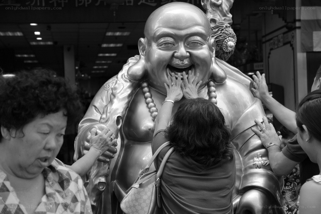 People touching a laughing Buddha statue