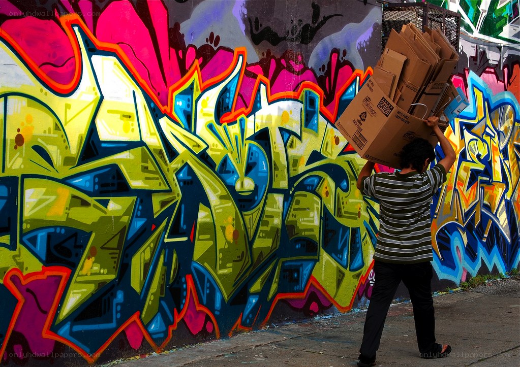 Person carrying boxes past graffiti wall