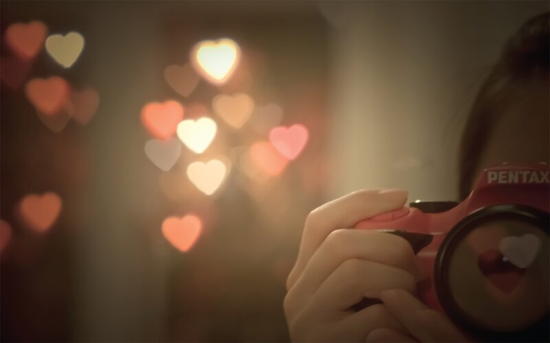 person holding camera with heart bokeh