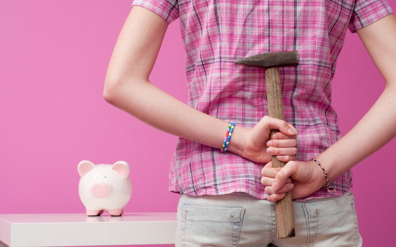 Person holding hammer near piggy bank