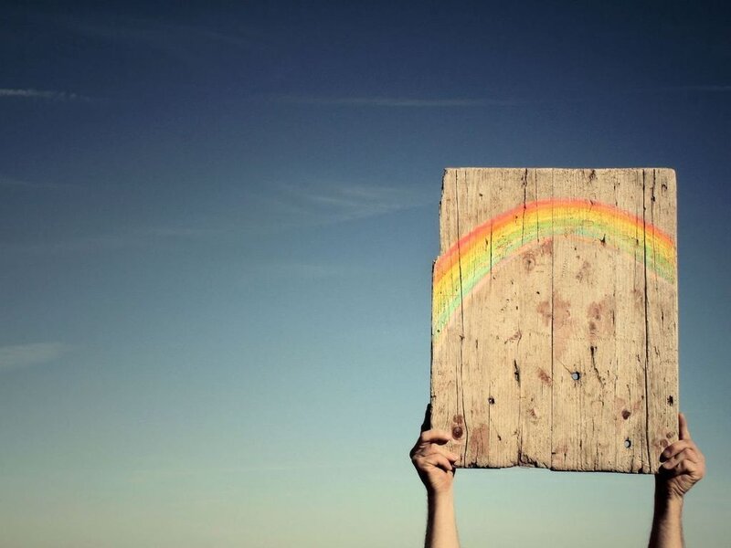 person holding wooden sign with rainbow