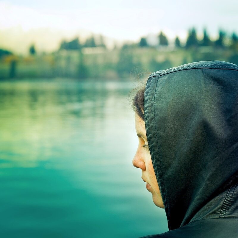 person in hood by lake