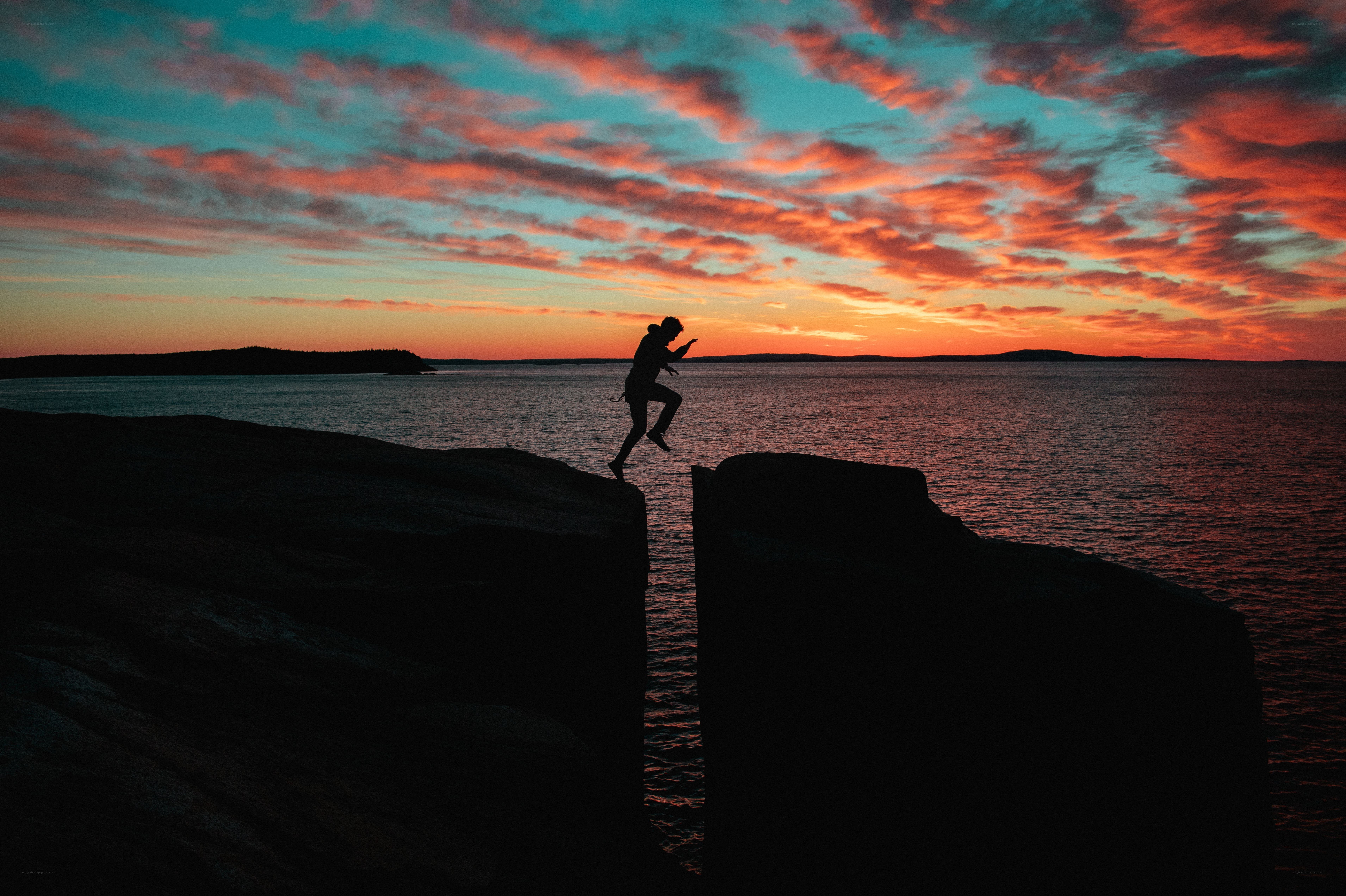 Person jumping between rocks at sunset