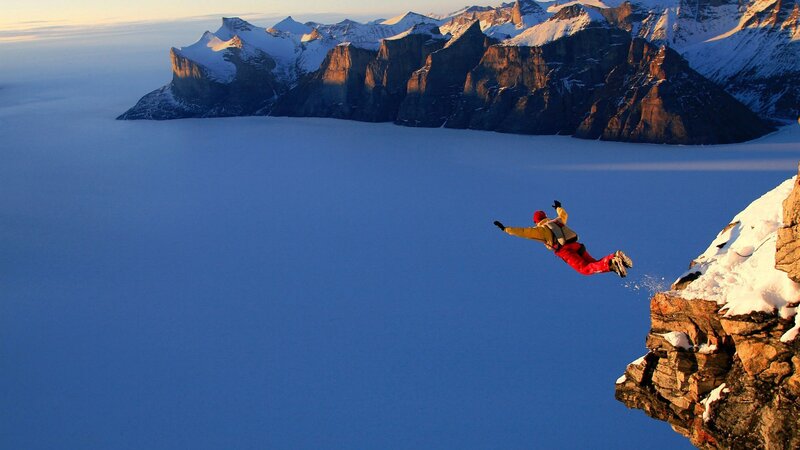 person jumping from snowy cliff