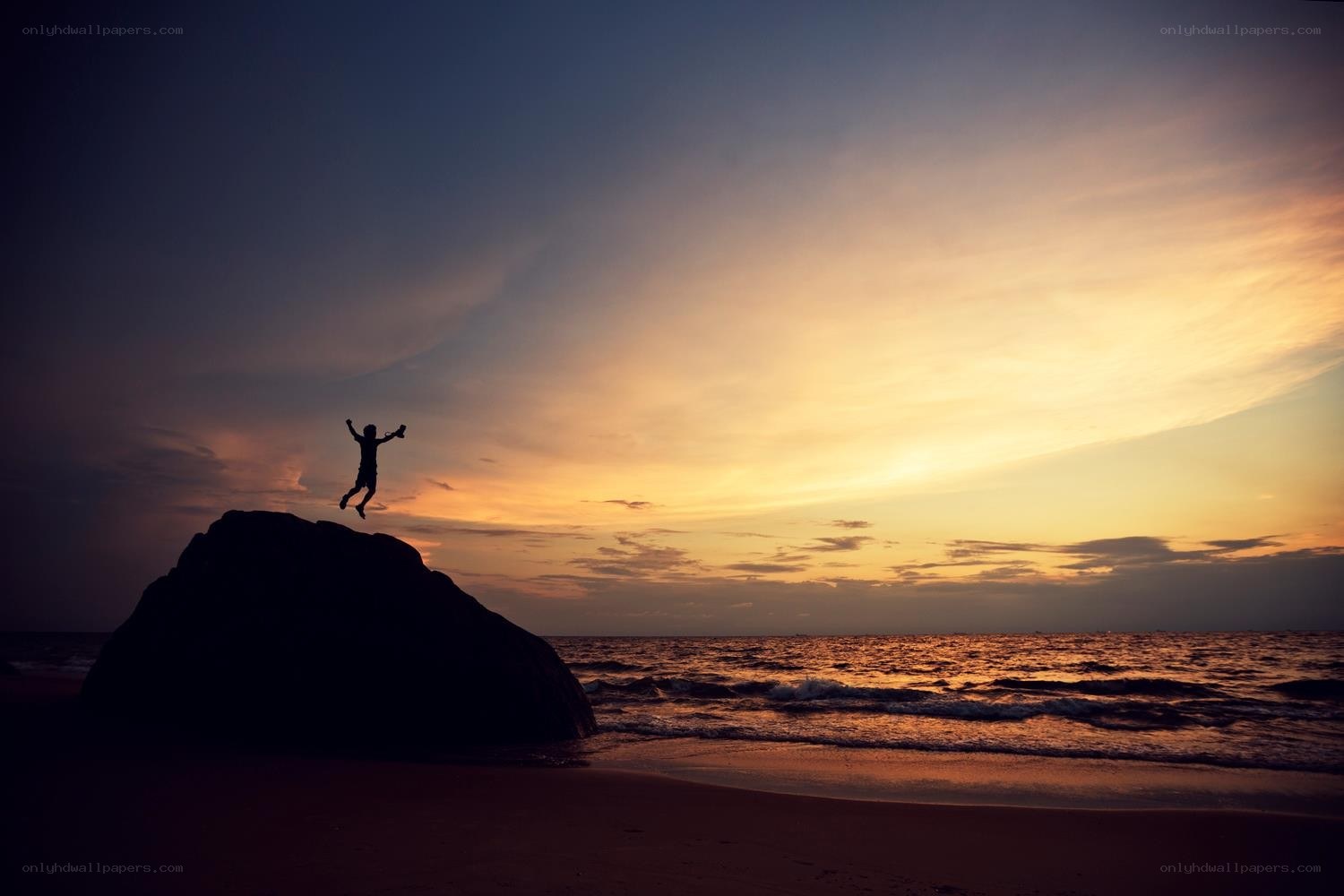Person jumping off rock at sunset