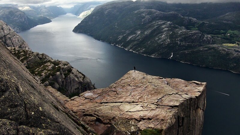 person on a cliff overlooking a fjord