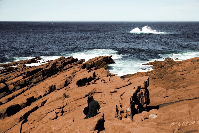 Person on rocky coast with iceberg