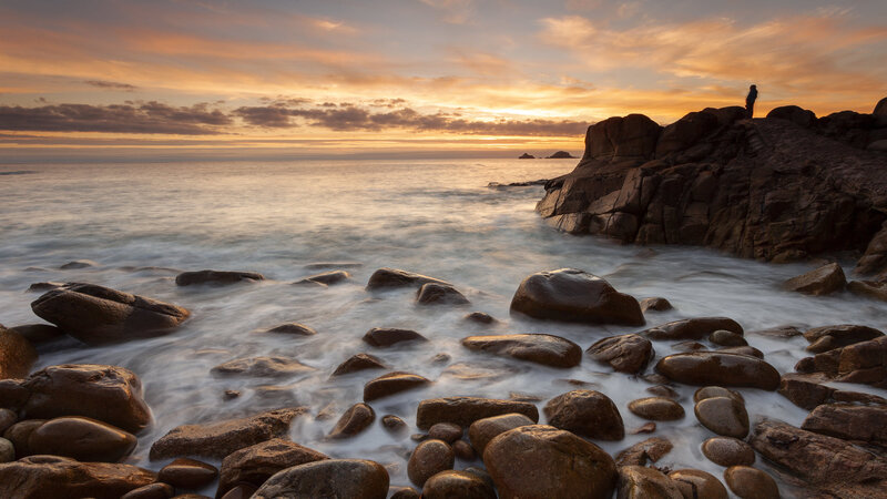 Person on Rocky Shore — Orange, Serene, Sunset, Photograph, Rocks