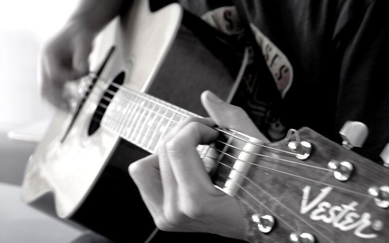 Person Playing Acoustic Guitar — Black, Focused, Photograph, Hands, Shirt