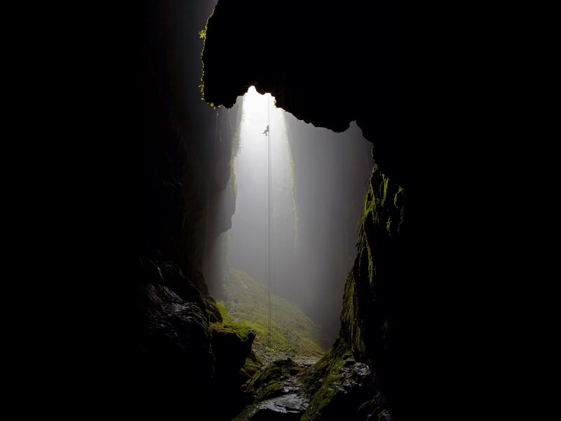 Person Rappelling in Cave — Black, Dramatic, Photograph, Light Beam, Moss