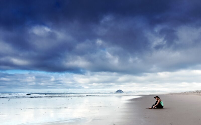 Person sitting on beach under stormy sky