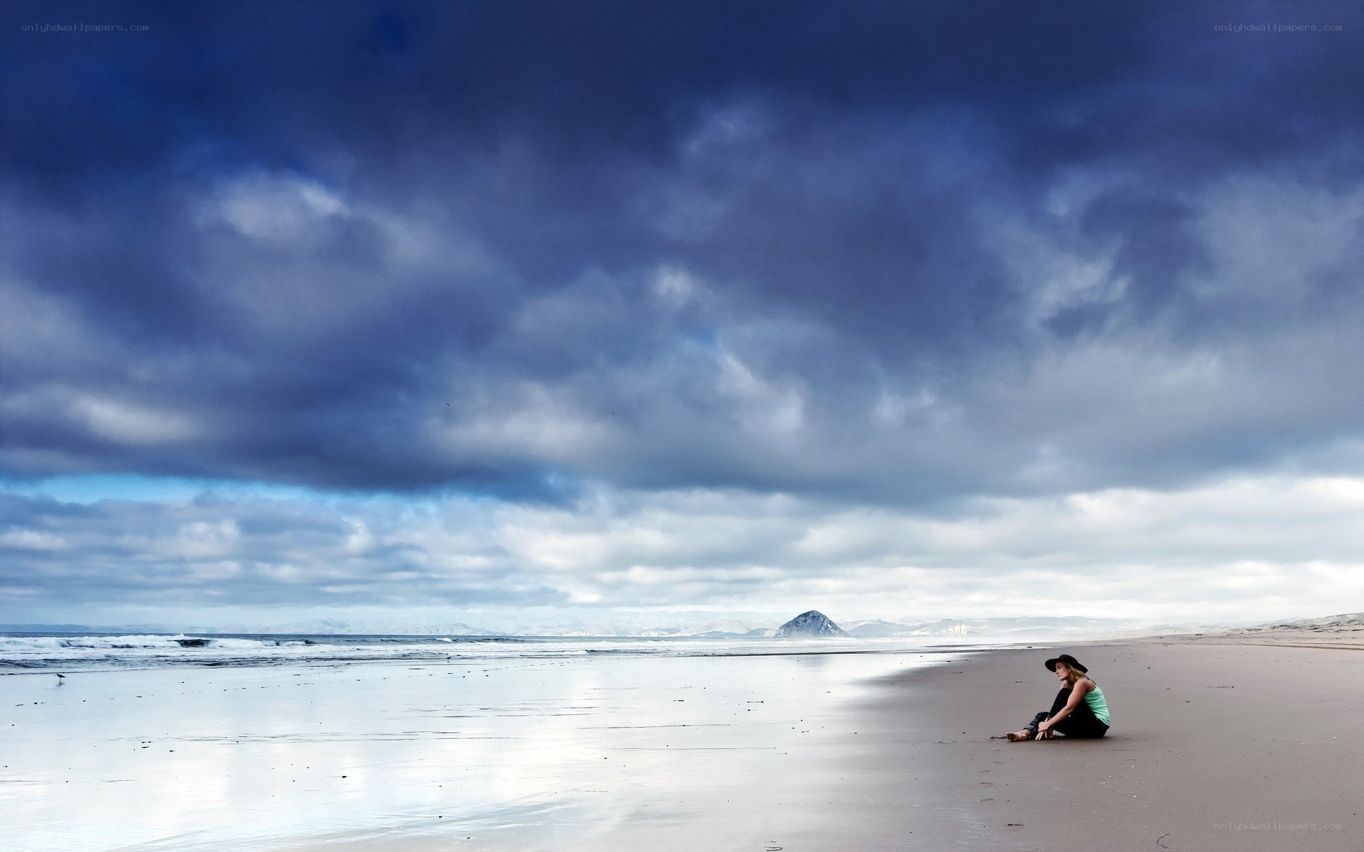 Person sitting on beach under stormy sky