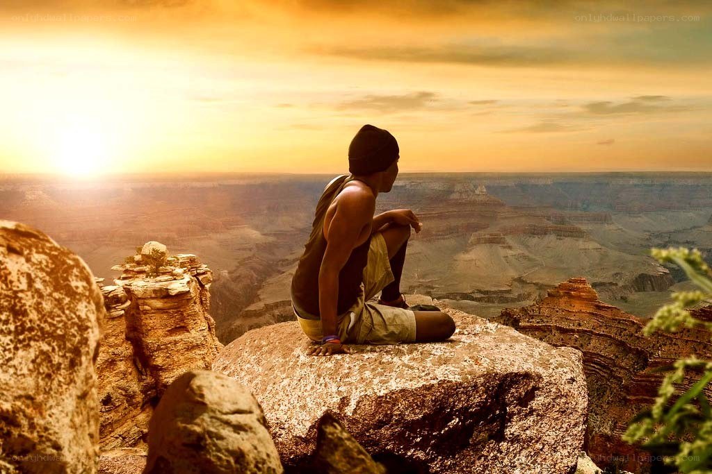 person sitting on cliff at sunset