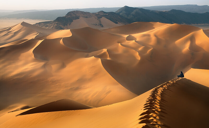 Person Sitting on Sand Dune — Orange