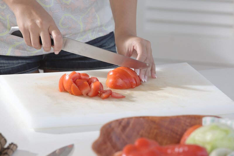 person slicing tomato on cutting board
