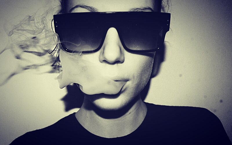 person wearing sunglasses exhaling smoke