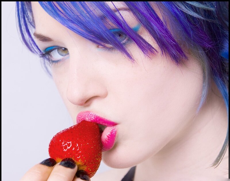 person with colorful hair eating strawberry