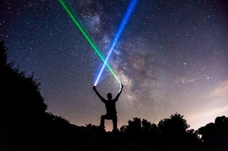 Person with laser lights under stars