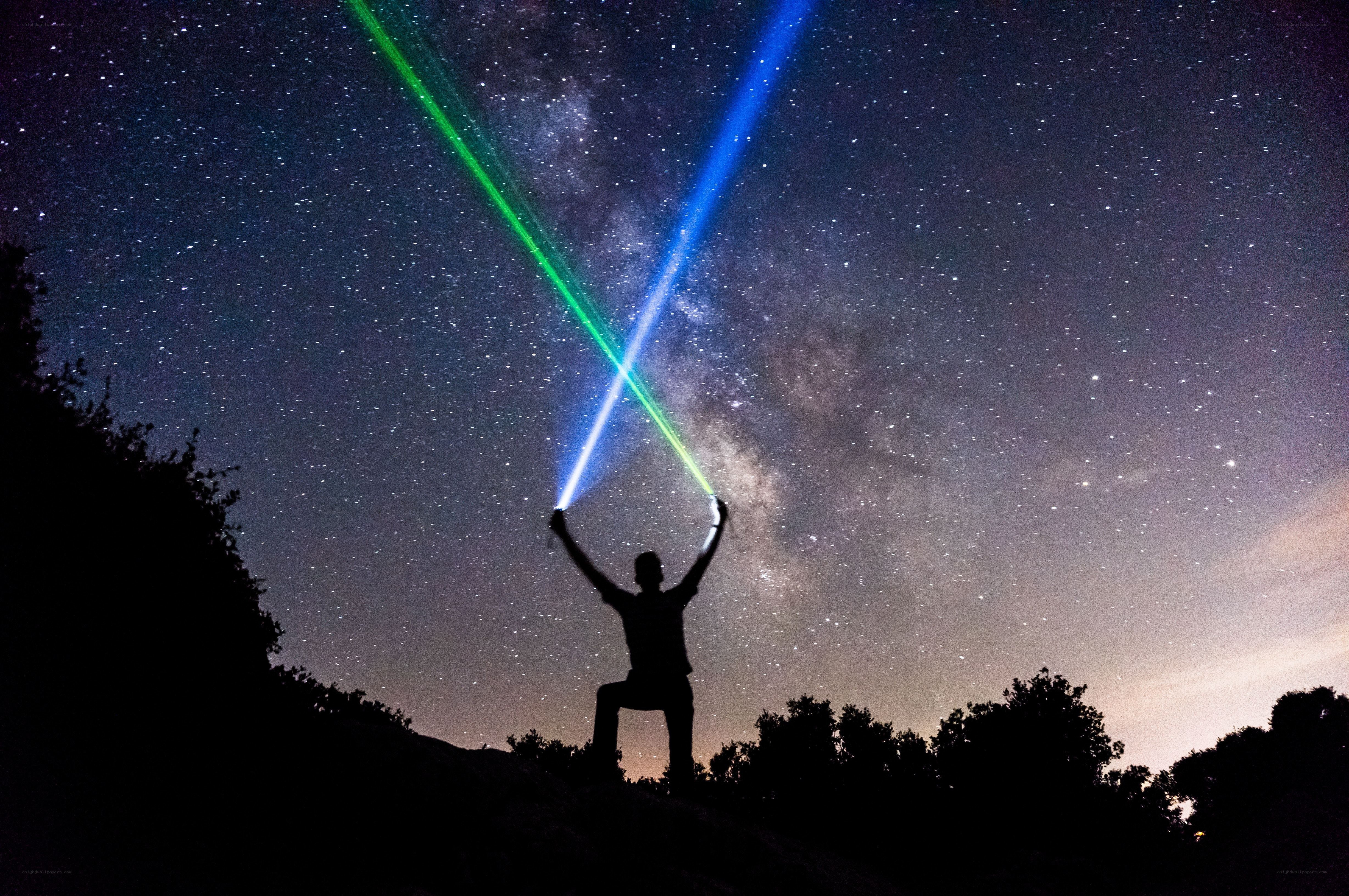 Person with laser lights under stars