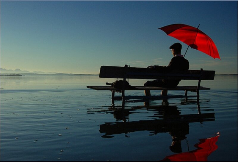 Person with red umbrella on bench