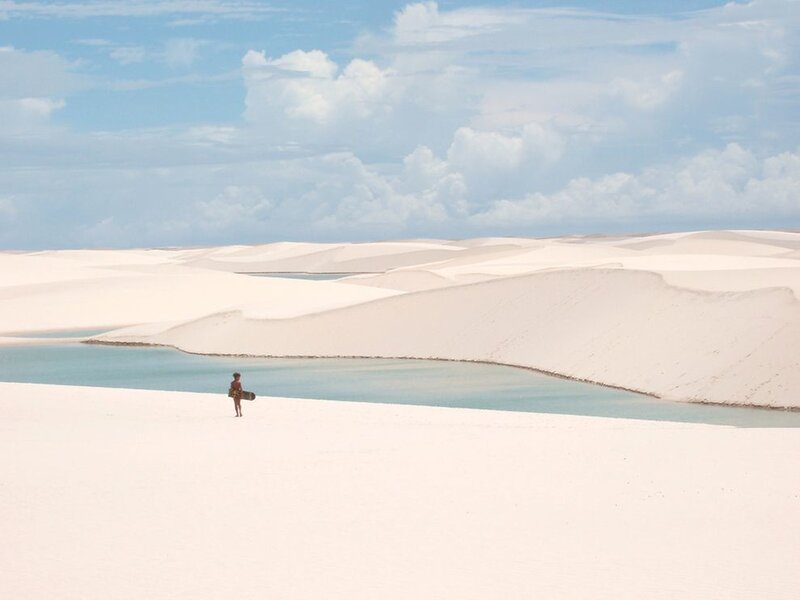 Person with surfboard on sand dunes