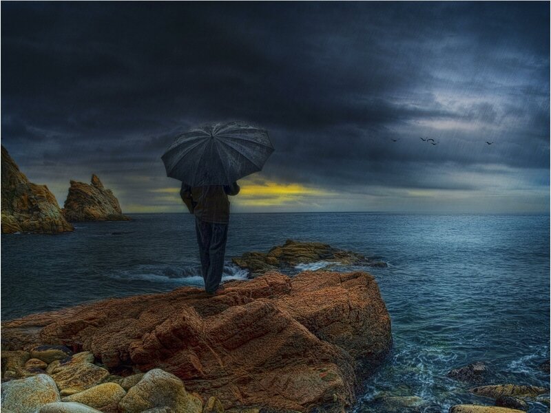Person with umbrella on rocky shore