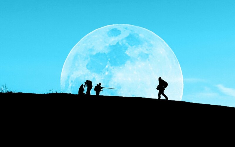 Photographers silhouetted against moon