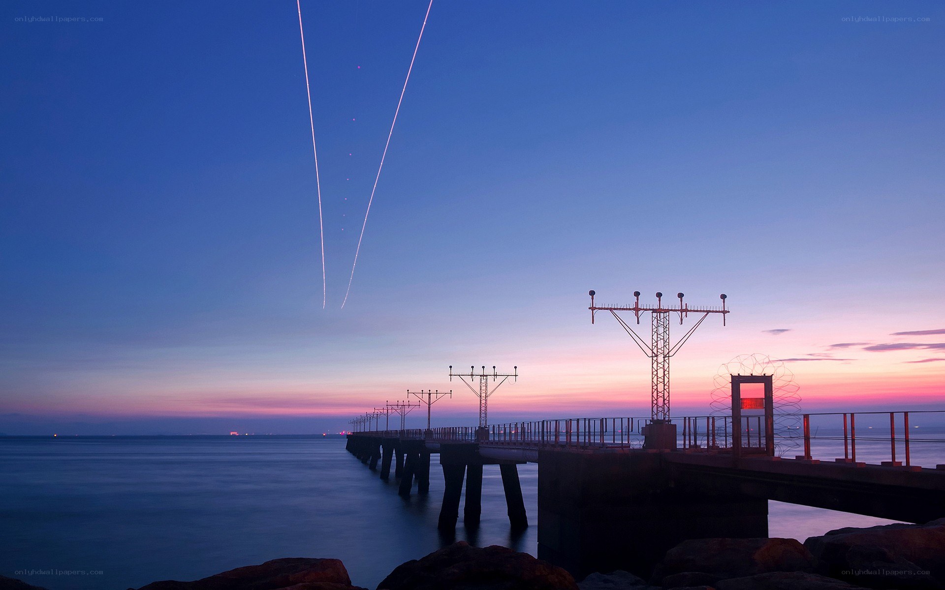 Pier at twilight with airplane trails