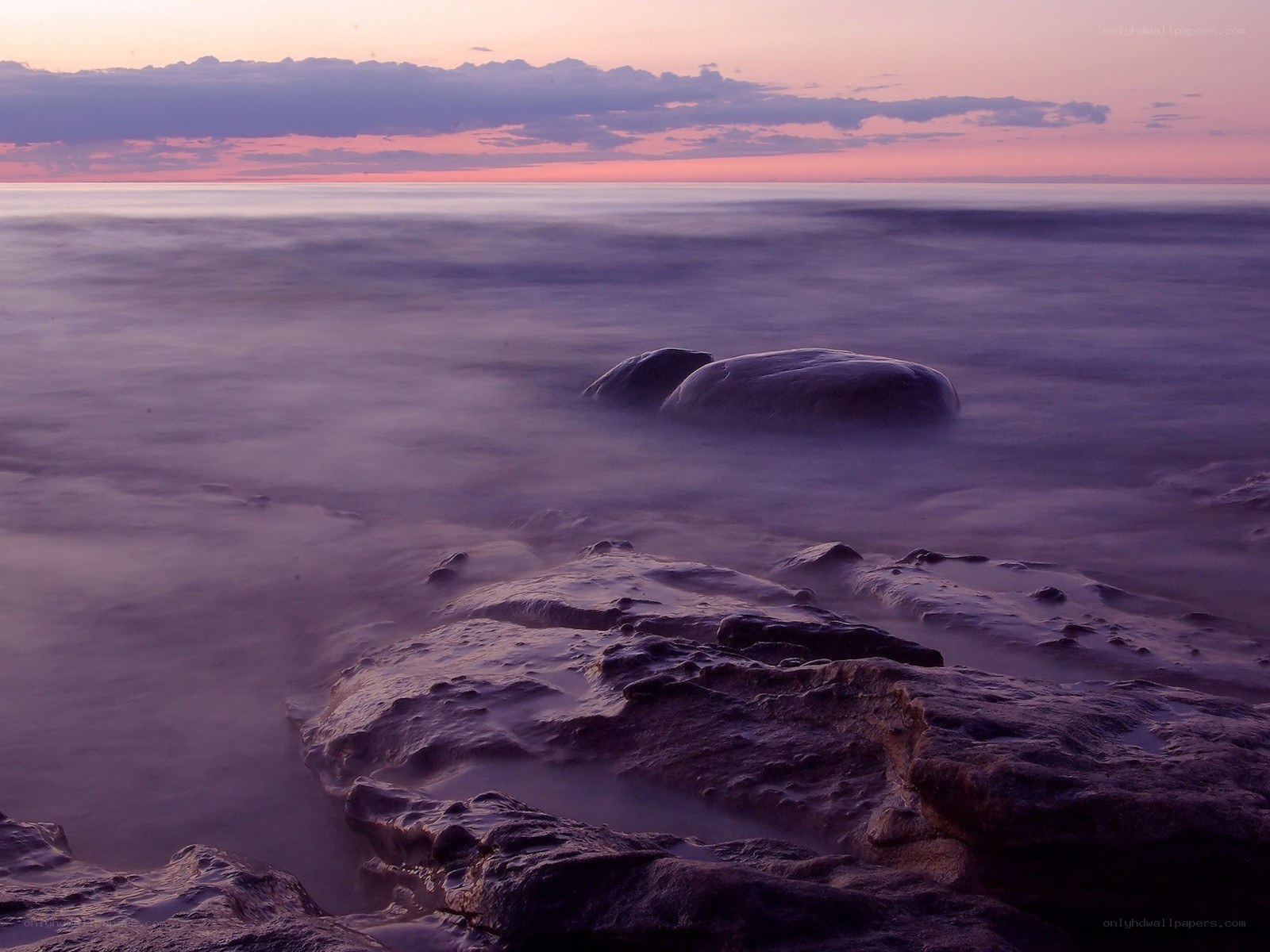 Purple sunset over ocean rocks