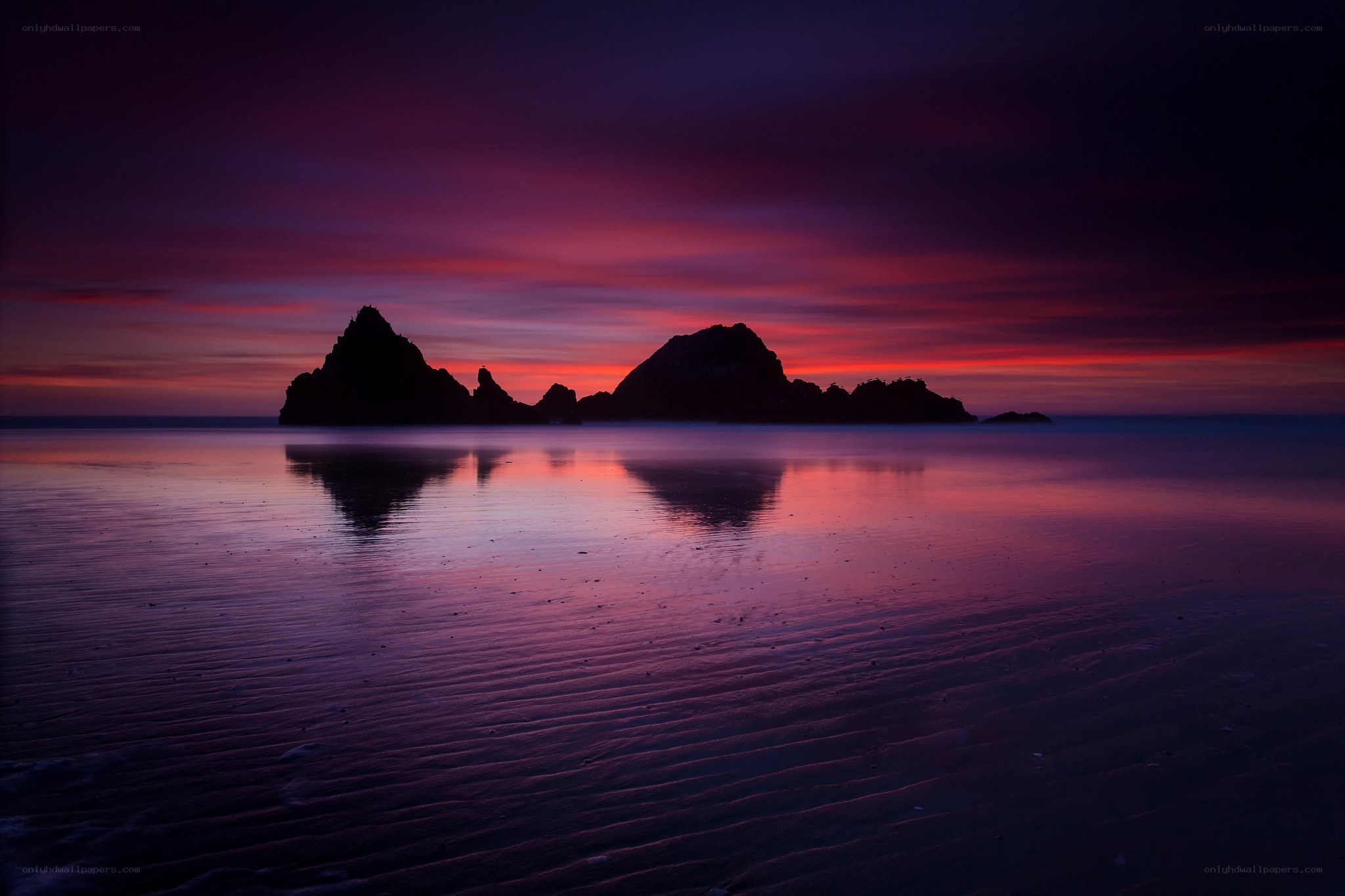 Purple sunset over ocean rocks